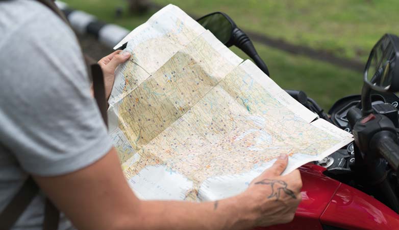 A man checks a map while on a motorcycle adventure, seeking directions outdoors.