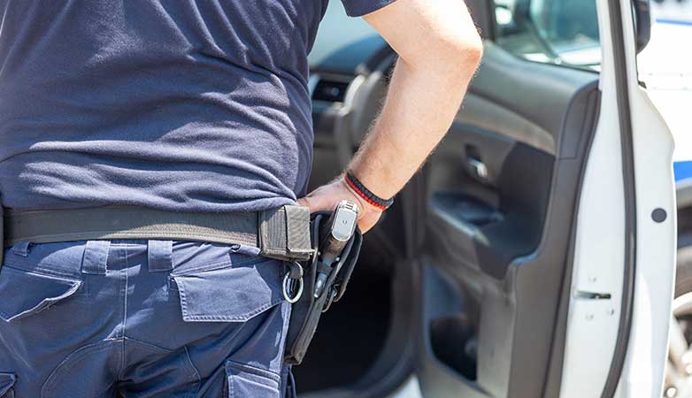 A man stands next to his car with a holstered gun.
