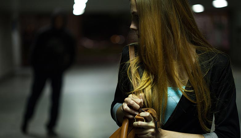 Woman holds on to her bag as a suspicous figure follows her at night.