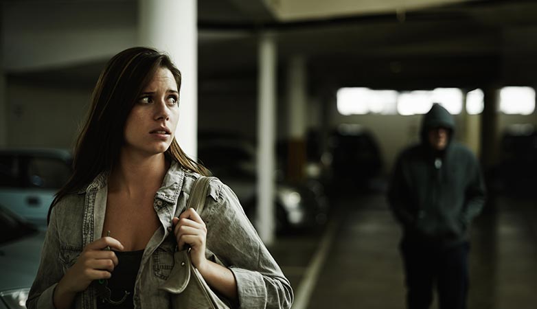 Woman walking in a parking garage with a man in a hoodie behind her.